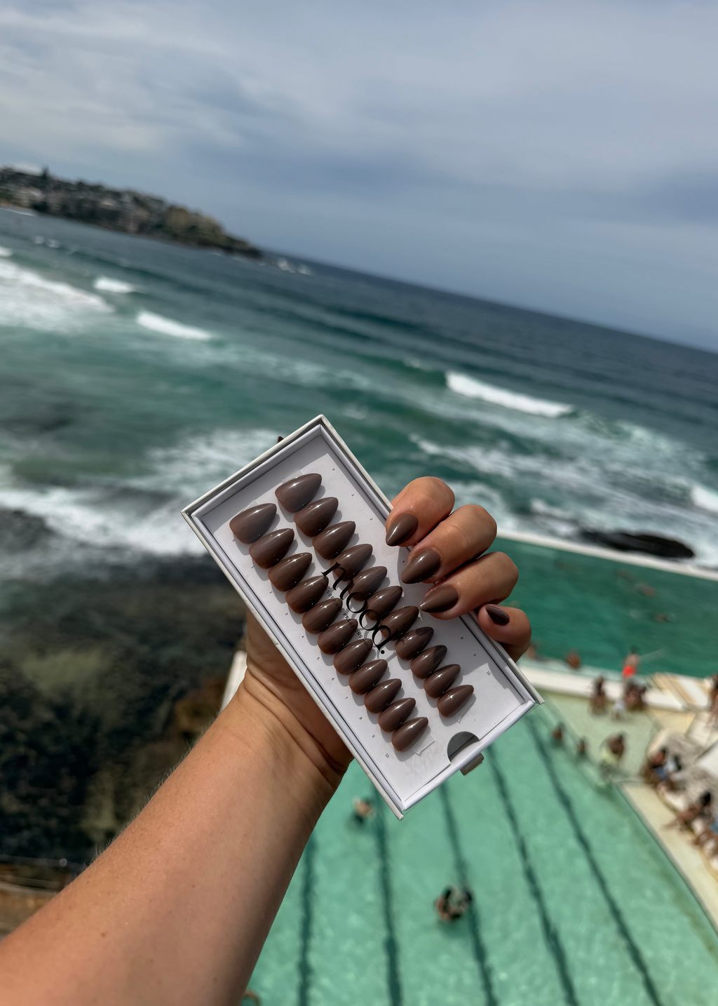 Hand holding a press on nails with ocean and beach in the background